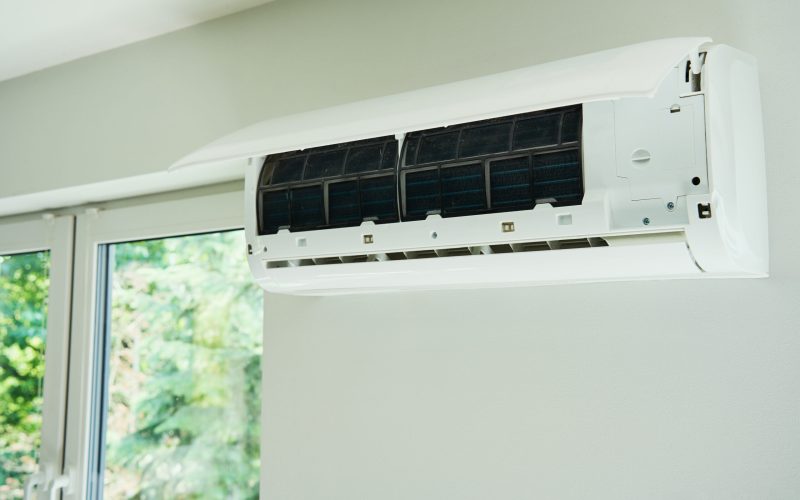 White air conditioner unit is mounted on wall, ready for maintenance. Climate system with opened front cover revealing internal components. Repairing HVAC in apartment