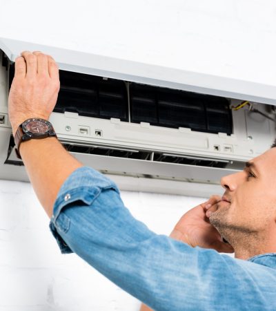 handsome man talking on smartphone while repairing air conditioner
