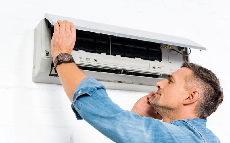 handsome man talking on smartphone while repairing air conditioner