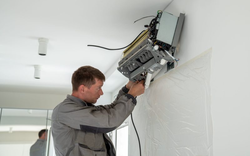 Man technician worker in uniform fixing repairing apartment air conditioner, installing wall-mounted mini split. AC unit maintenance concept